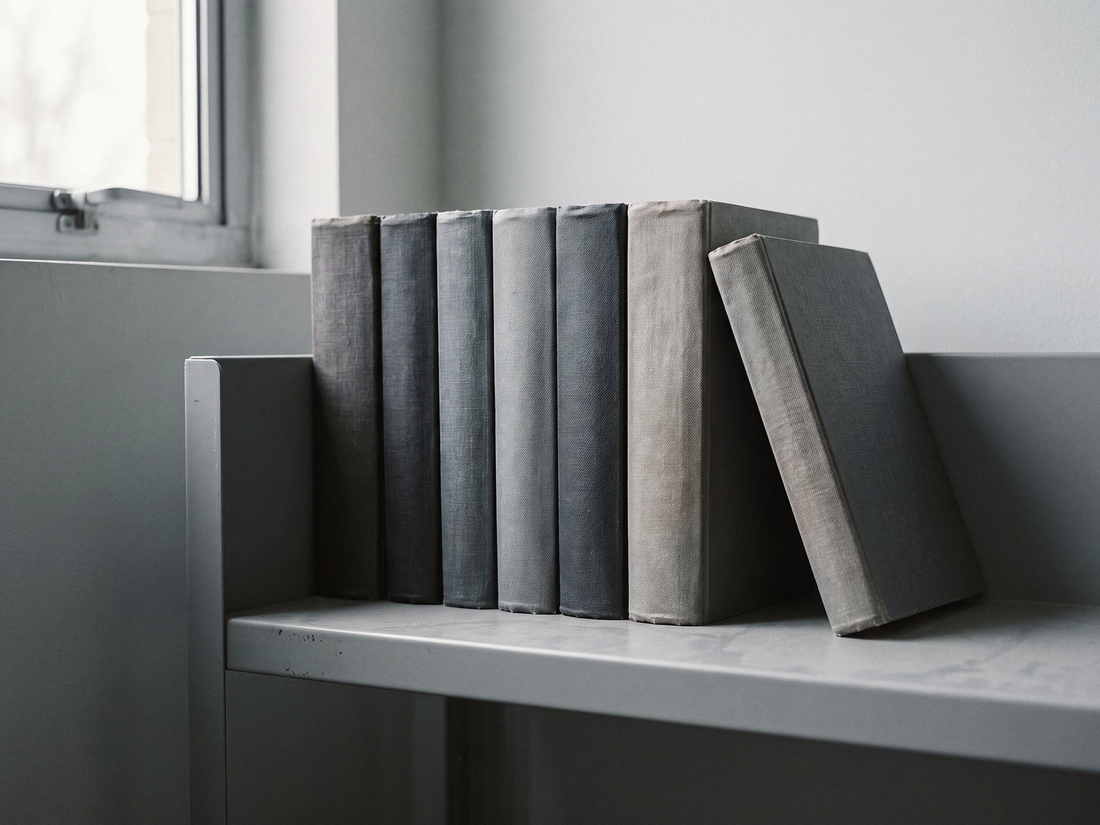 A row of cloth-bound reference volumes with blank spines on a steel shelf in daylight.