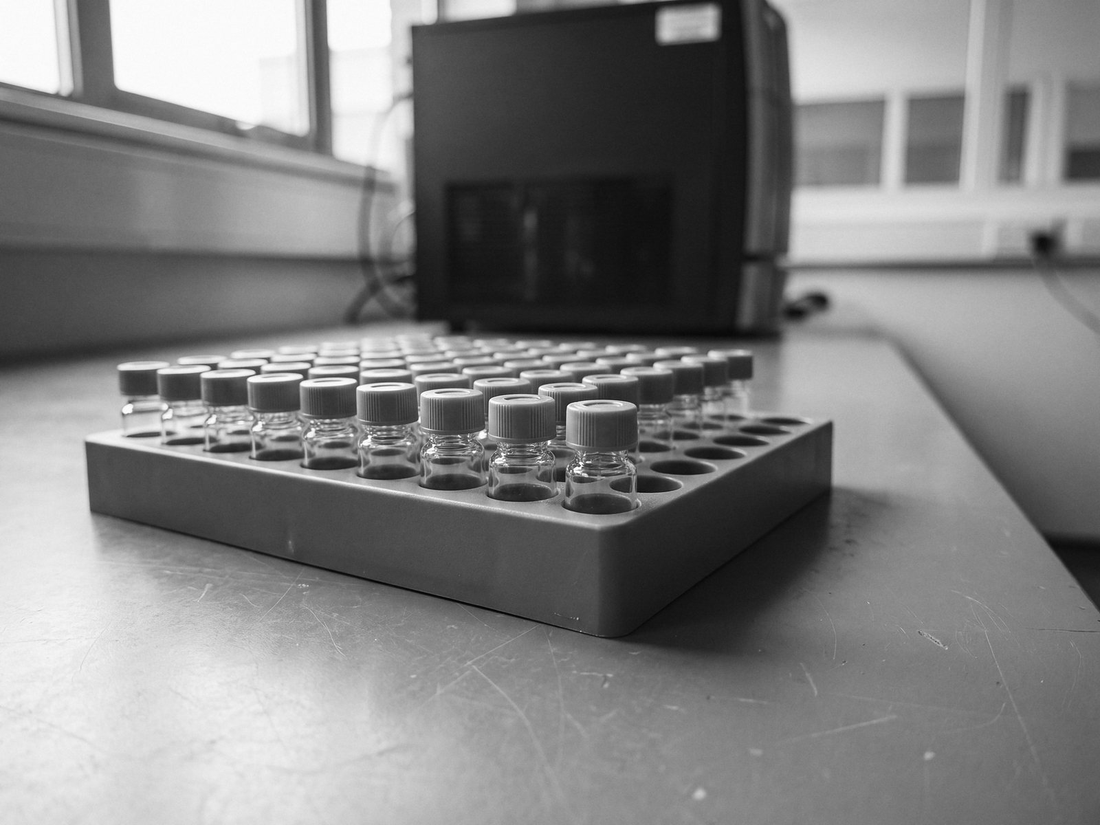 Black-and-white close view of a tray of small capped glass sample vials on a laboratory bench.